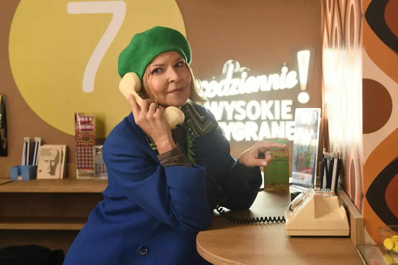 Kobieta w zielonym beretku rozmawia przez telefon, wskazując na zdrapki. Czy to tajemnica, dlaczego sprzedawcy w kolekturach wykupują konkretne numery zdrapek?