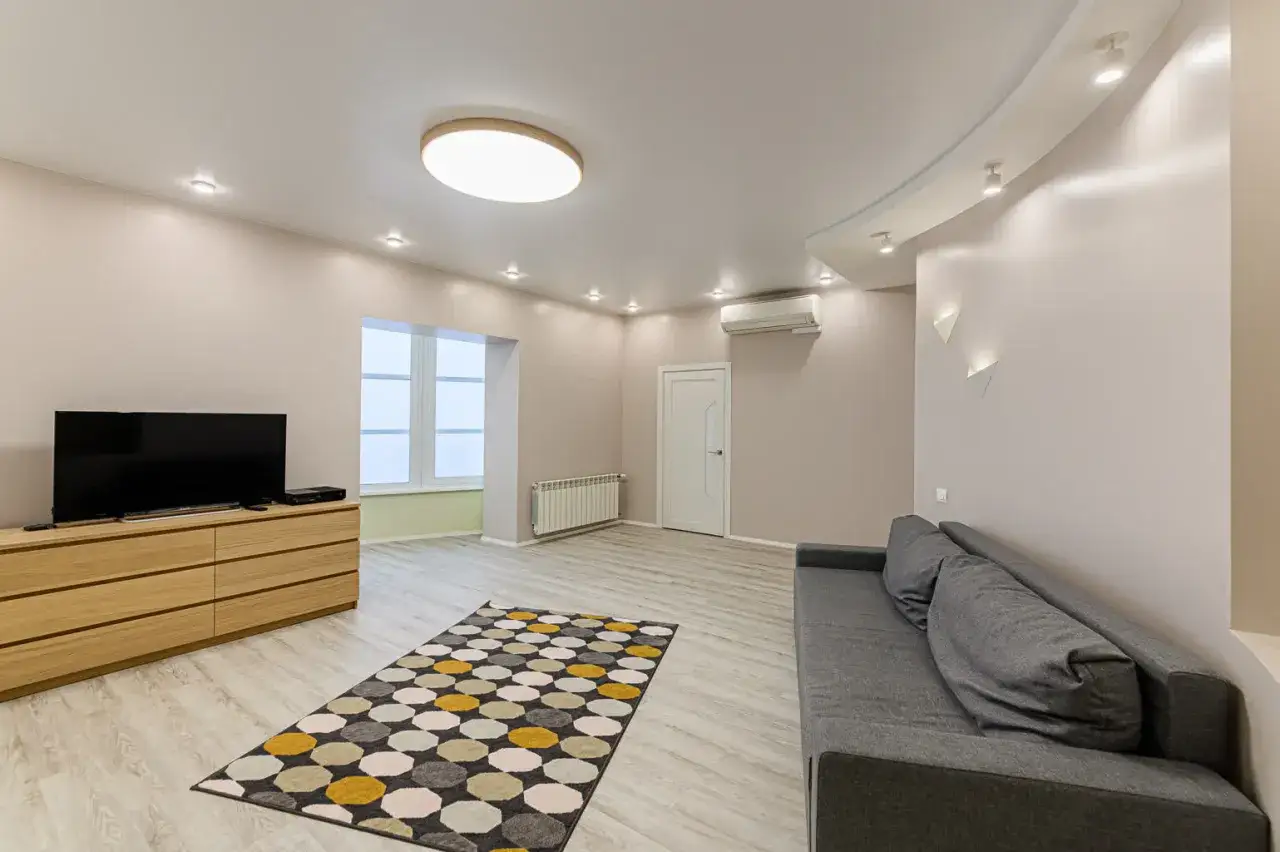 Nowoczesny salon z szarą kanapą, drewnianą komodą i telewizorem. Zastanawiasz się, jaka moc żarówki led do salonu będzie najlepsza?