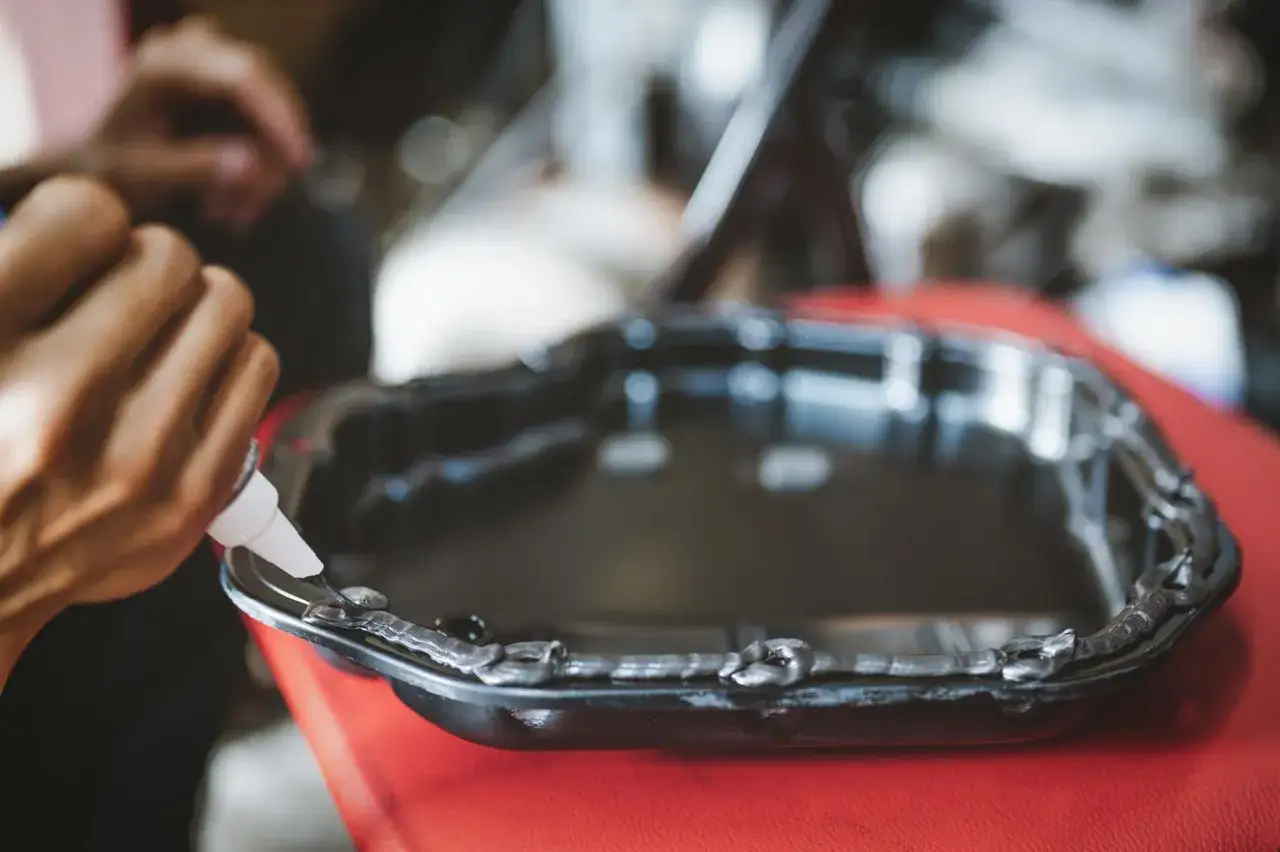 Nakładanie silikonu samochodowego na miskę olejową. Czas schnięcia silikonu zależy od warunków.