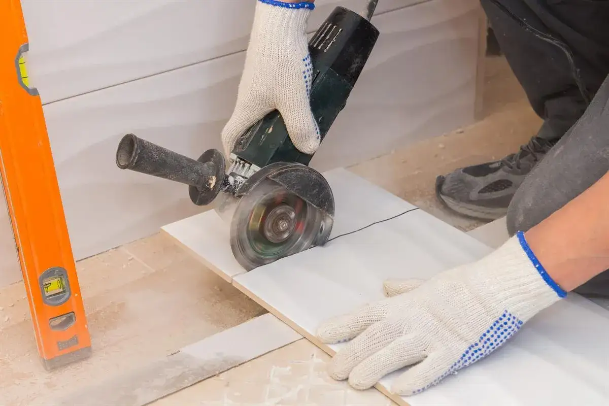 Rękawice ochronne i szlifierka kątowa pomagają w precyzyjnym cięciu płytek. Poziomica obok wskazuje na dokładność pracy.