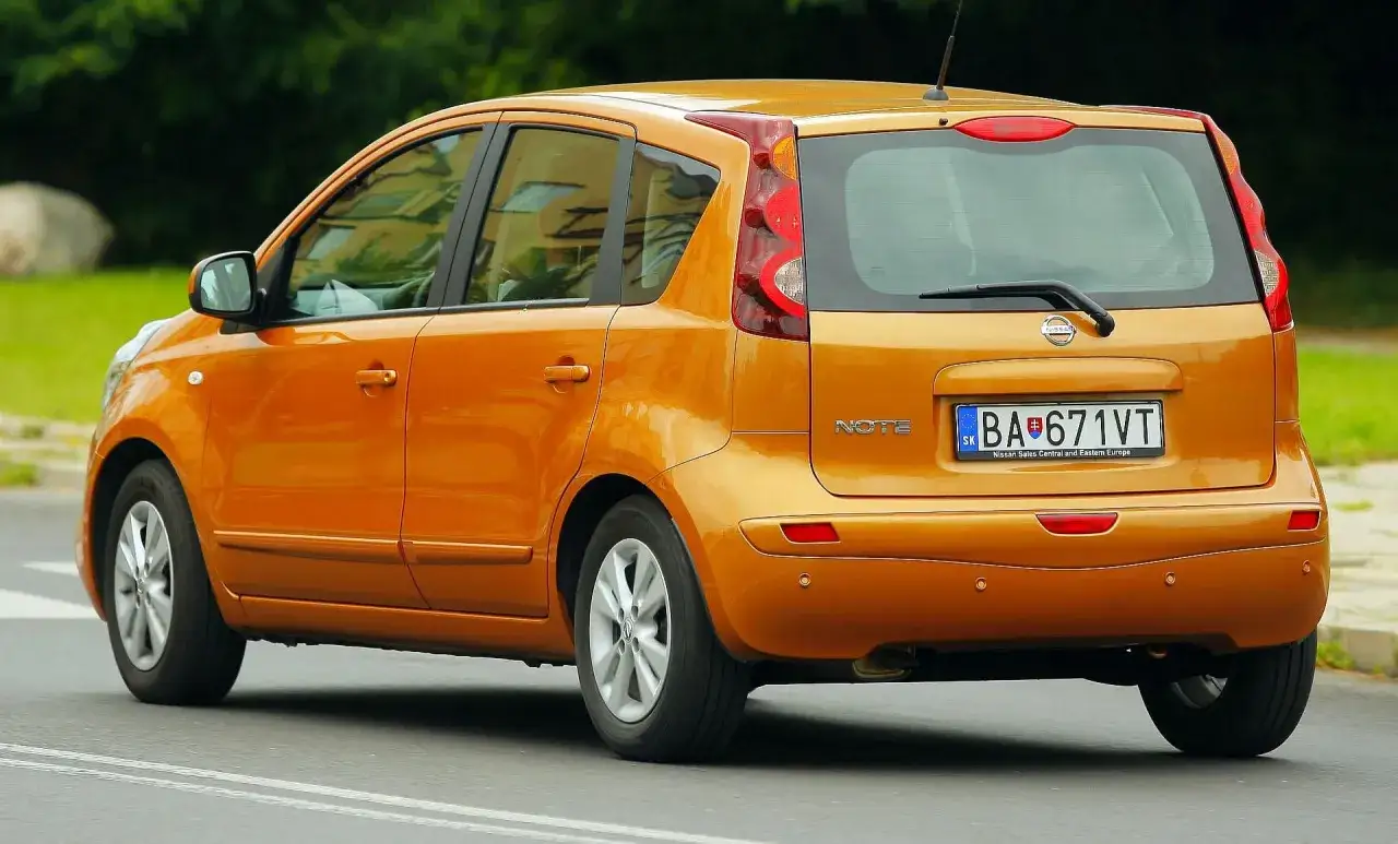 Pomarańczowy Nissan Note z tablicą rejestracyjną BA 671VT jedzie po drodze.