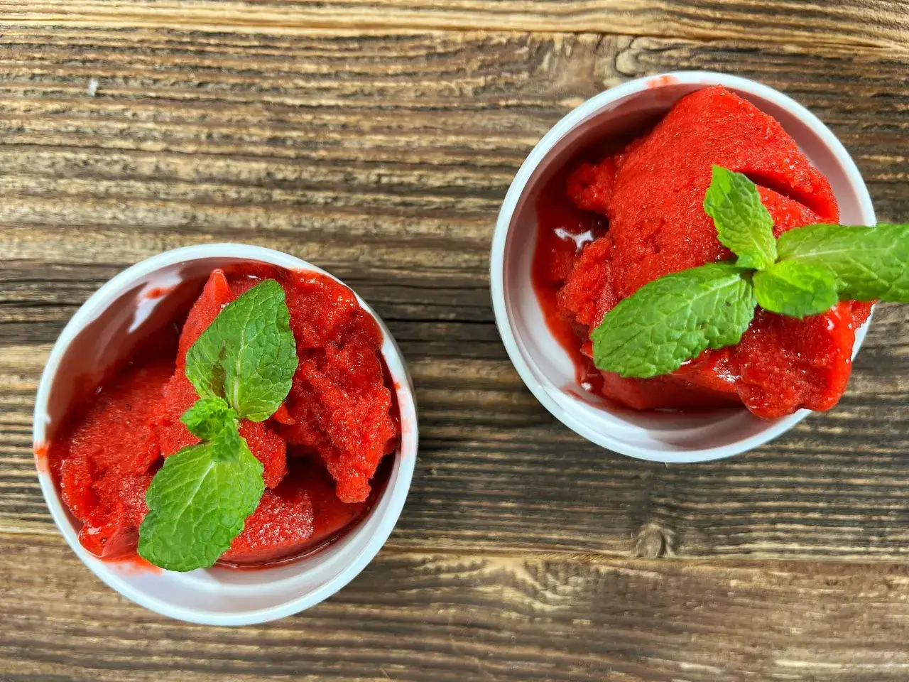 Dwa pucharki z orzeźwiającym sorbetem truskawkowym z mrożonych truskawek, ozdobione listkami mięty. Idealny przepis na lato!