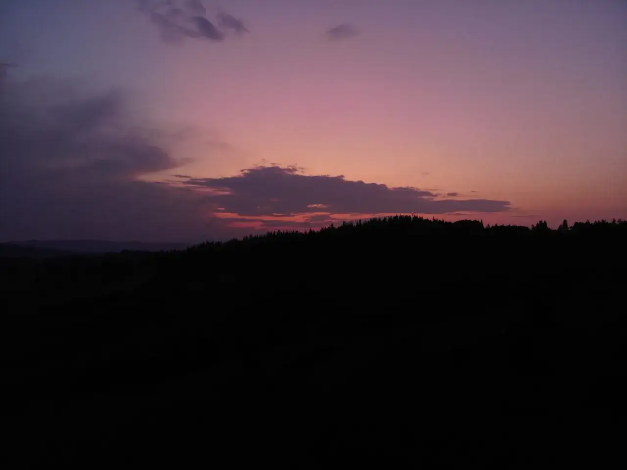 Zach&oacute;d słońca nad lasem na zboczu, gdzie widać stare wierchy Turbacz. Fioletowe niebo z chmurami.