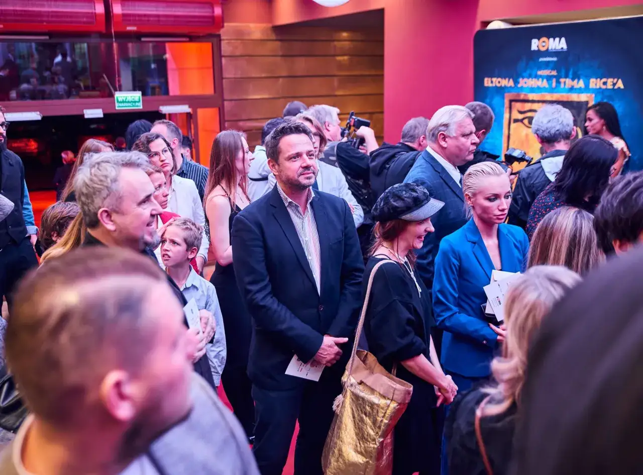 Tłum ludzi przed Teatrem Roma, wśród nich aktorzy i widzowie, oczekujący na spektakl.