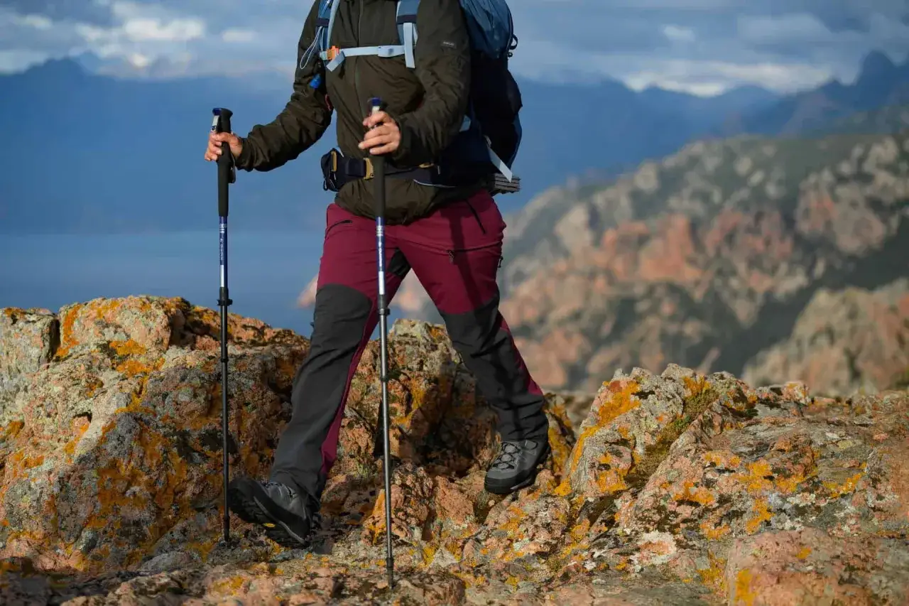 Osoba w g&oacute;rskich spodniach i kurtce używa kijki trekkingowe, by pokonać skalisty szlak. Idealne kijki w g&oacute;ry zapewniają stabilność.