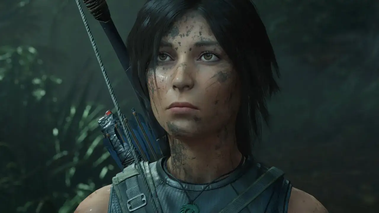 Nowy Tomb Raider: Lara Croft z łukiem i strzałami, ubrudzona ziemią, wpatruje się w mrok dżungli.