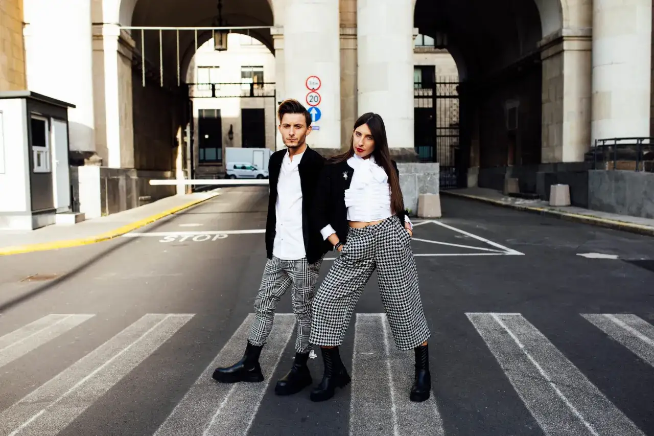 Para na pasach stojąca w spodniach w pepitkę. Stylowe, czarno-białe spodnie w kratkę tworzą modne stylizacje.