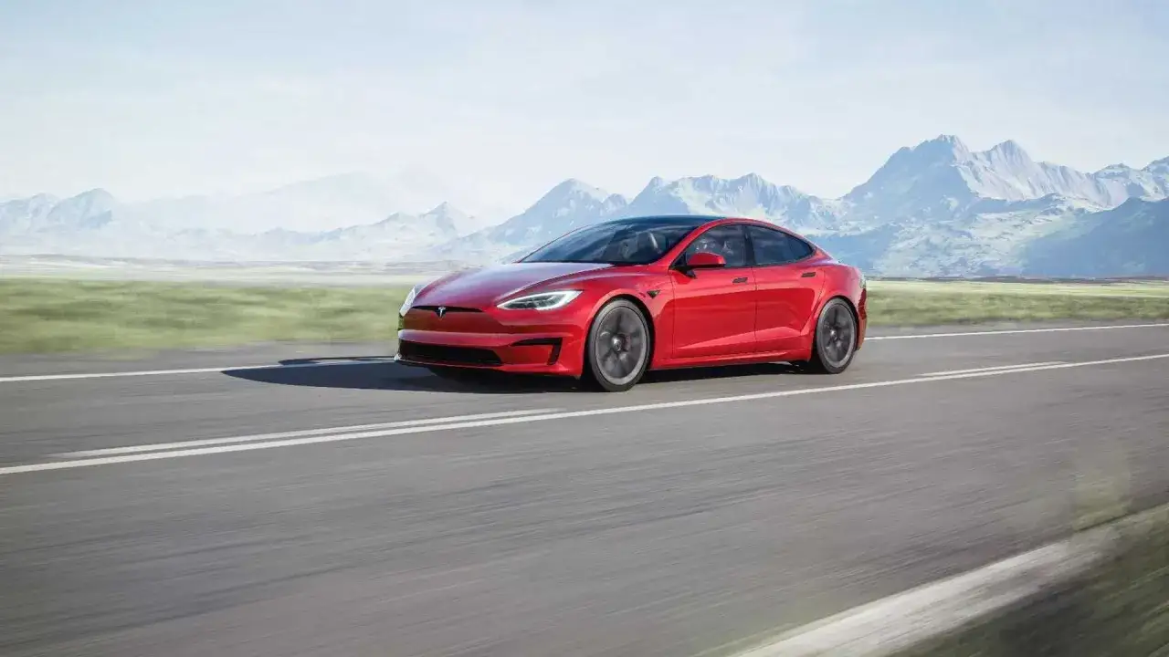 Czerwony Tesla Model S z imponującą mocą, pędzący po pustej drodze z g&oacute;rami w tle.