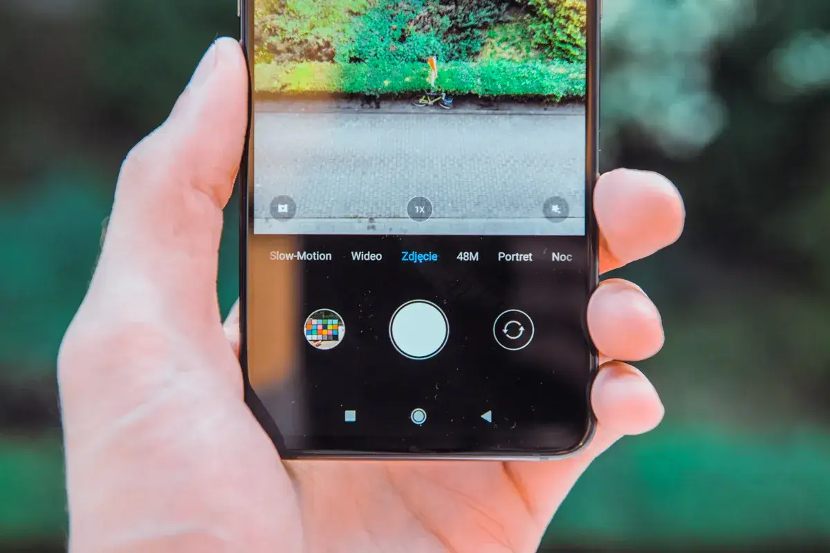 Dłoń trzyma smartfon Xiaomi, na ekranie kt&oacute;rego widać interfejs aparatu z opcjami: Slow-Motion, Wideo, Zdjęcie, 48M, Portret, Noc.
