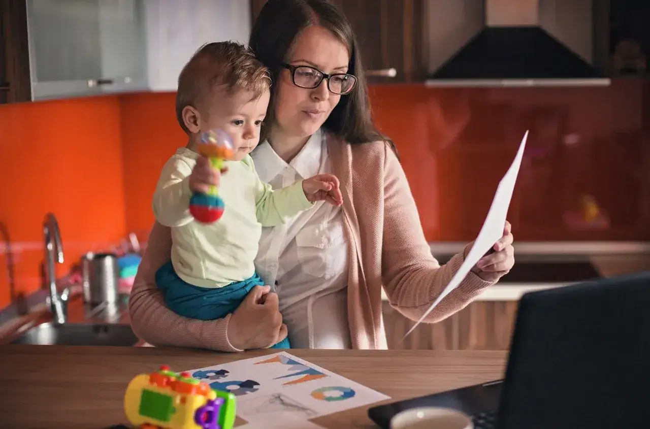 Kobieta z dzieckiem na rękach analizuje dokumenty, szukając informacji o ubezpieczeniu zdrowotnym na macierzyńskim po ustaniu zatrudnienia.