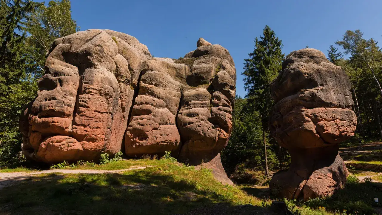Imponujące formacje skalne w G&oacute;rach Żytawskich, przypominające gigantyczne rzeźby, otoczone zielenią drzew.