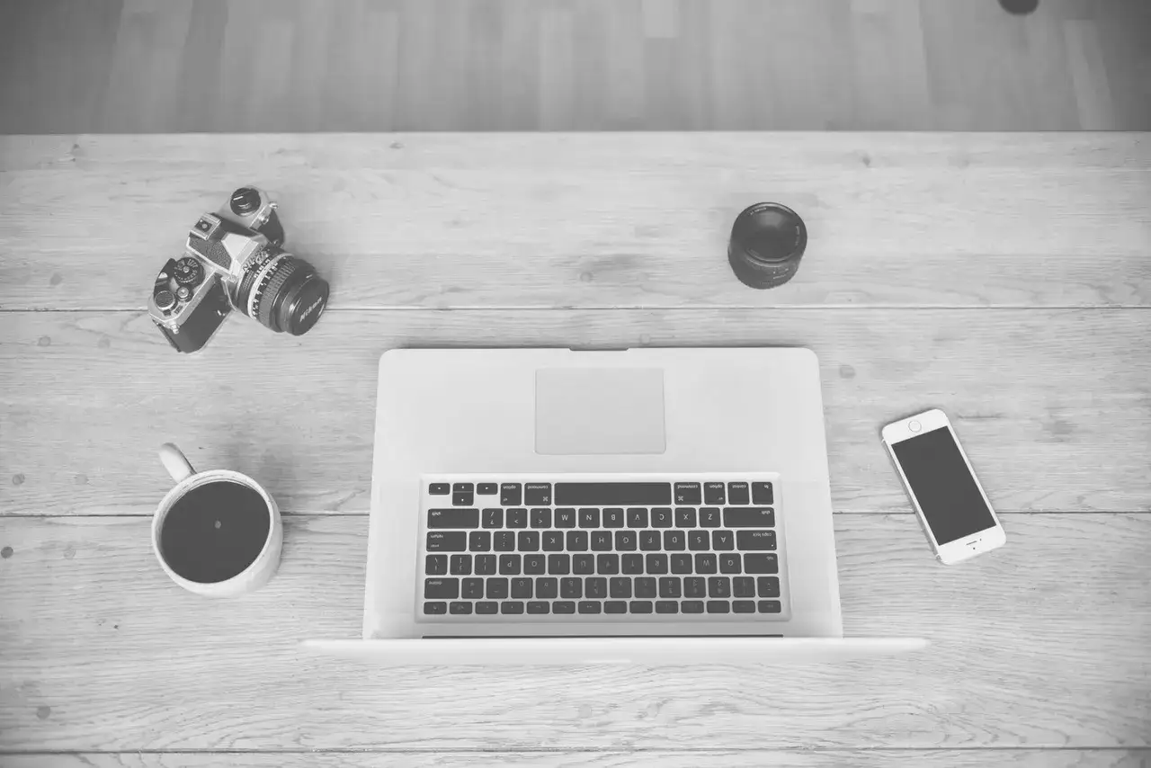 Kawa, aparat, laptop i telefon – idealny zestaw do nauki, jak zostać fotografem.
