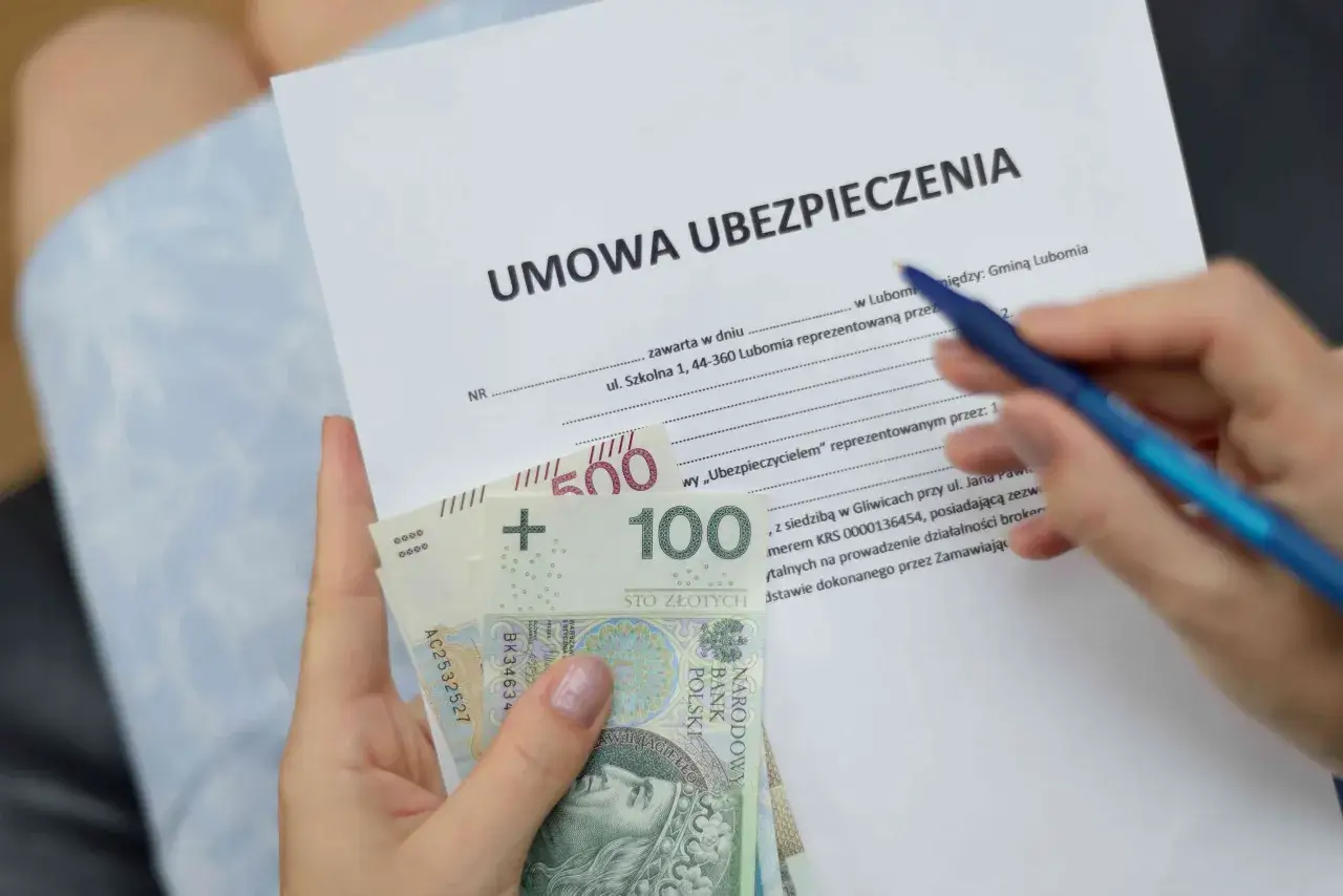 Umowa ubezpieczenia domu wymaga dokumentów i pieniędzy. Na zdjęciu widać umowę ubezpieczenia, polskie banknoty 100 i 500 zł oraz długopis.