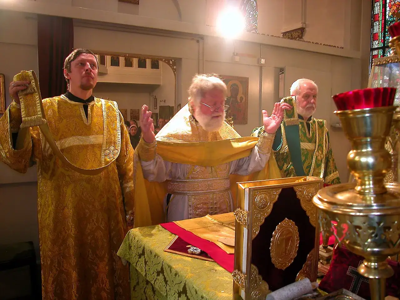 Trzech duchownych w bogato zdobionych szatach podczas iii modlitwy eucharystycznej. Przed nimi księga liturgiczna i świecznik.