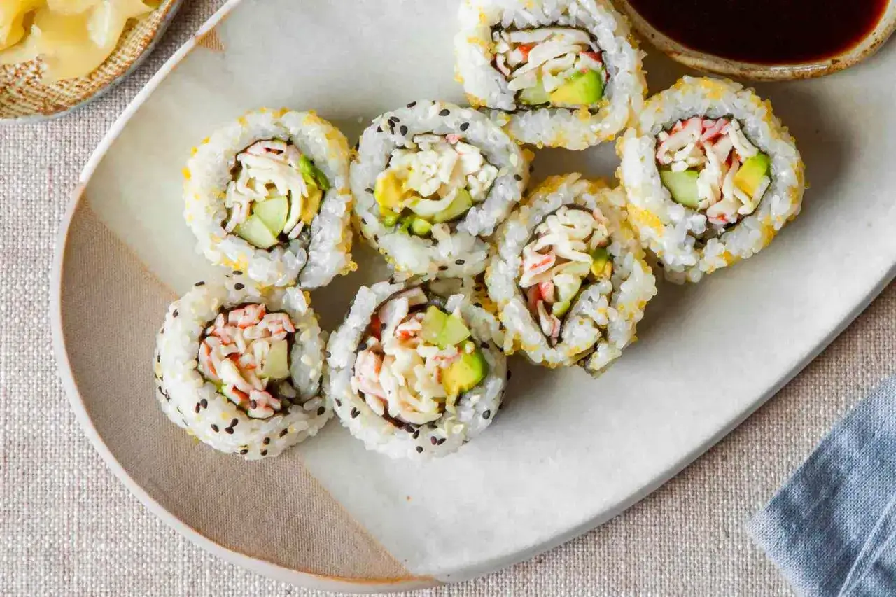 Siedem kawałków california roll sushi z awokado, ogórkiem i paluszkami krabowymi, posypane sezamem i ikrą.