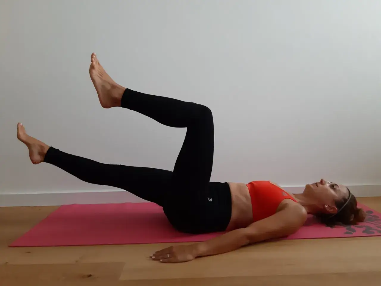 Kobieta wykonuje ćwiczenia na mięśnie głębokie, leżąc na macie i unosząc nogi.