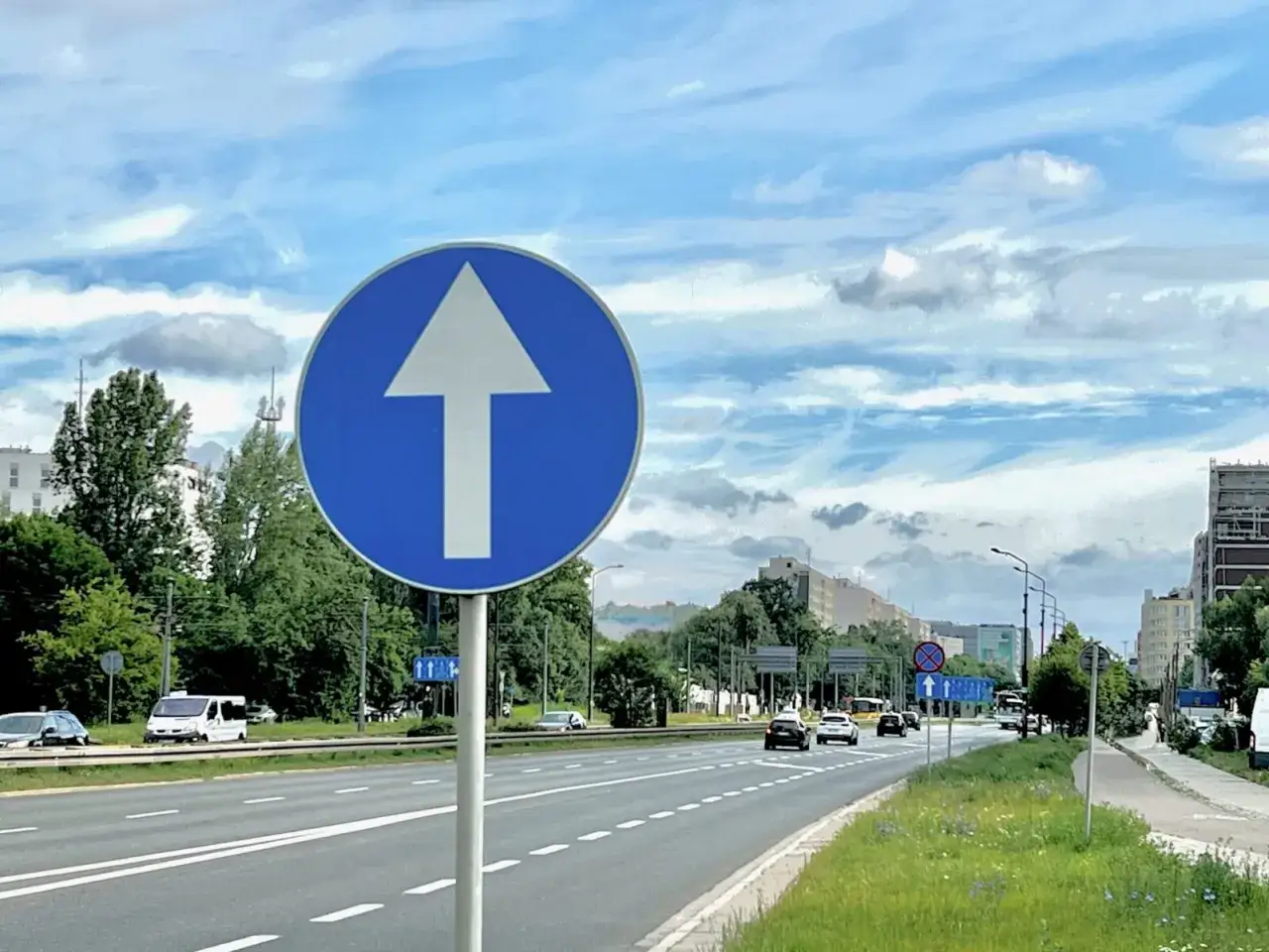 Znak nakazu jazdy prosto na drodze jednokierunkowej. Samochody jadą zgodnie z kierunkiem ruchu, unikając cofania.