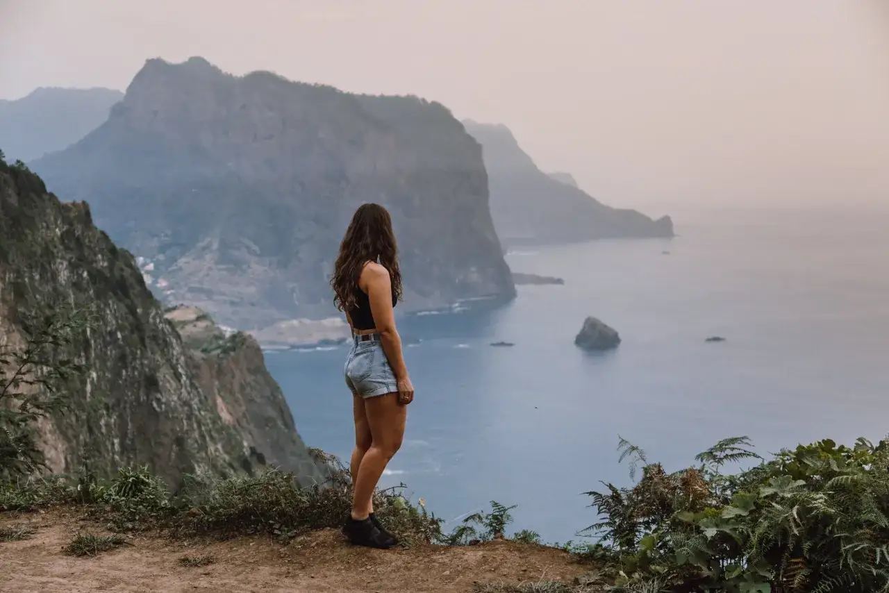 Kobieta na klifie podziwia mglisty krajobraz oceanu. Październikowa madera, mimo chmur, zachwyca surowym pięknem.