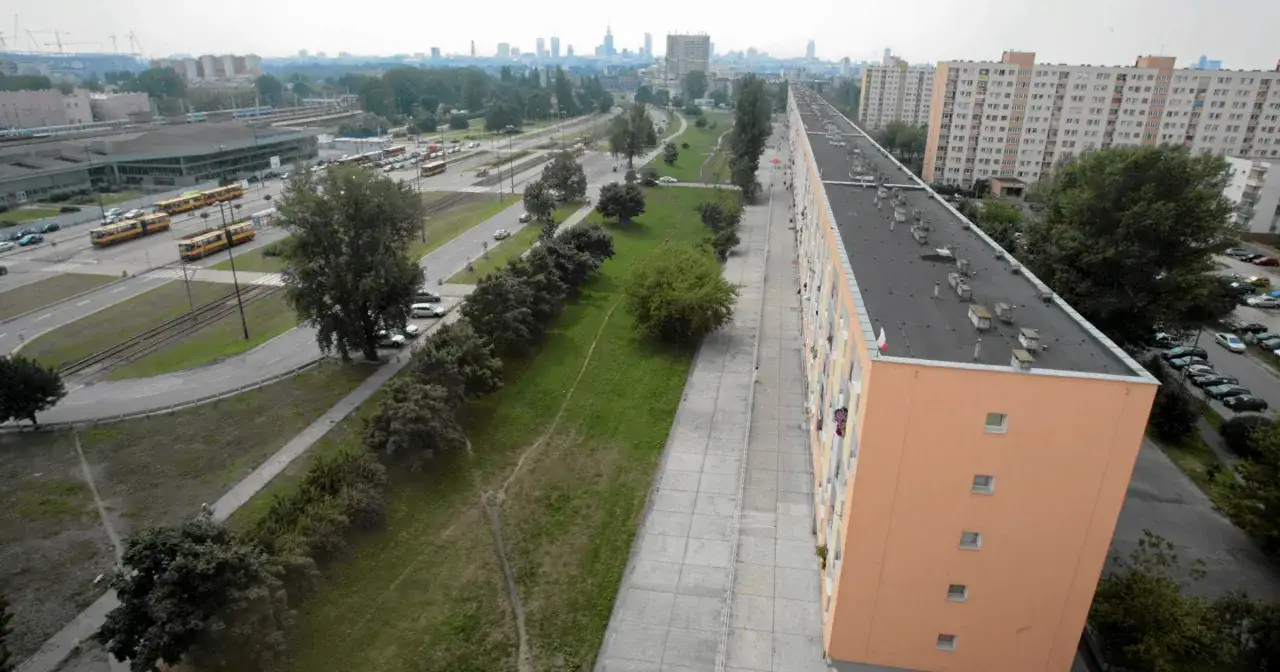 Długi, pomarańczowy blok mieszkalny, prawdopodobnie najdłuższy blok w Polsce, z widokiem na tory tramwajowe i panoramę miasta.