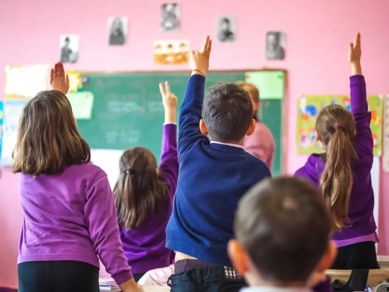 Dzieci z podniesionymi rękami, czekające na odpowiedź, kiedy nauczyciel nie może przeprowadzić lekcji.