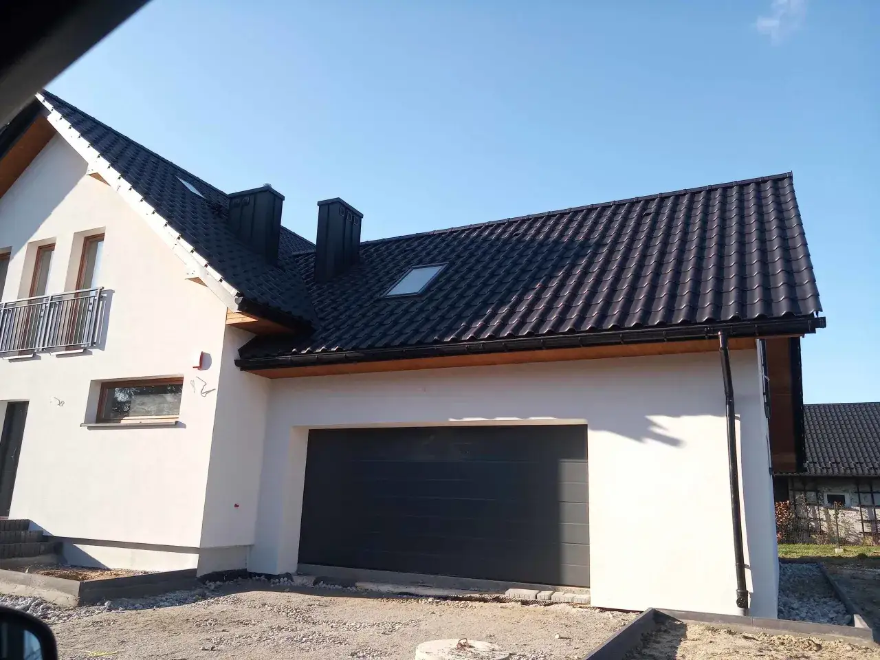 Nowy dom z białym tynkiem, ciemnym dachówką w kolorze antracyt i oknami w stylu winchester.