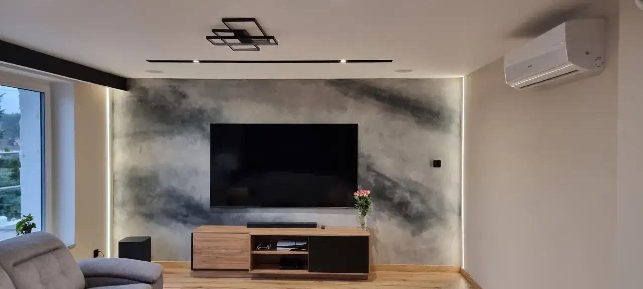 Nowoczesny salon z telewizorem na tle ściany z efektem betonu. Czy tynk dekoracyjny można malować? Tak, można go odświeżyć.