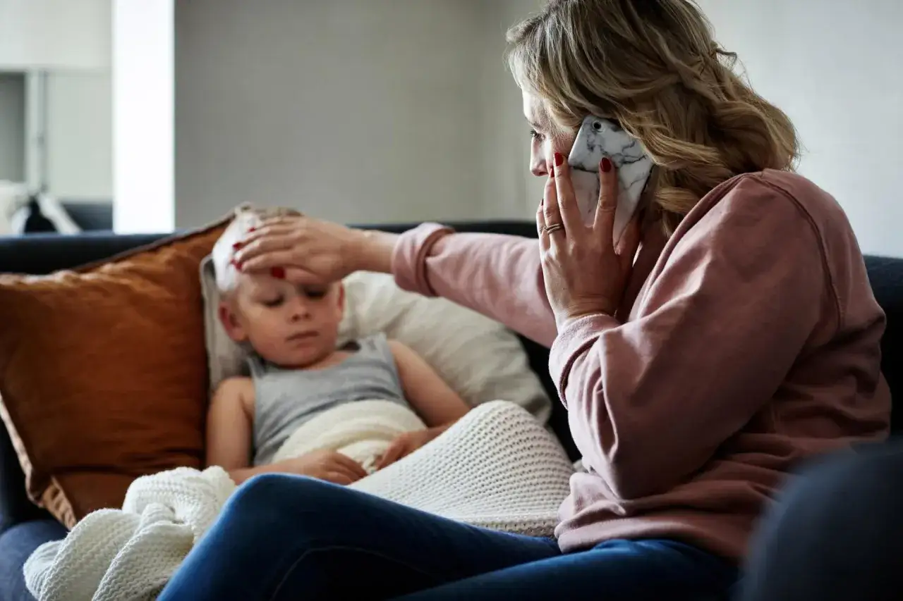 Matka z telefonem w ręku sprawdza gorączkę synka. Opieka nad chorym dzieckiem wymaga czujności i troski.