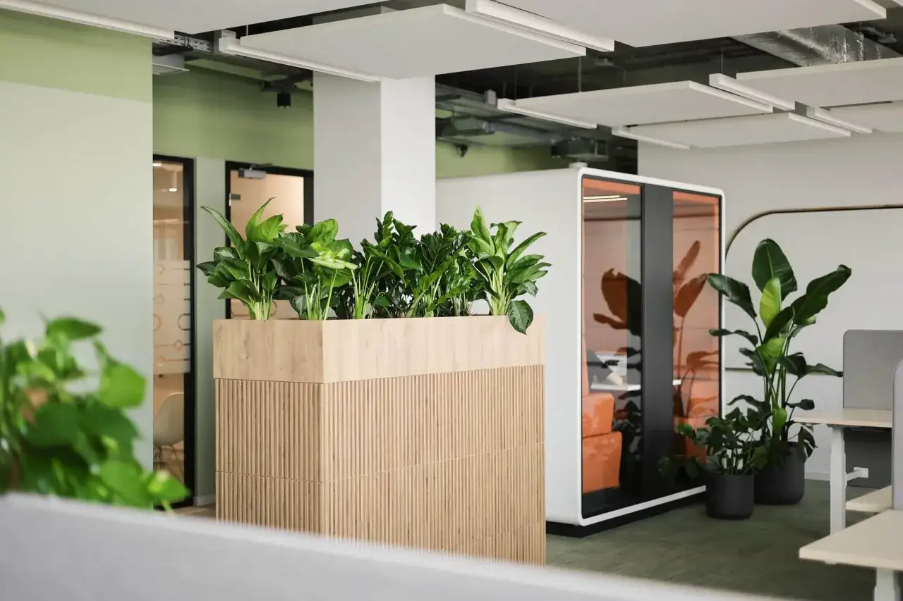 Nowoczesne biuro z zieloną ścianą roślin w drewnianej donicy. Obok znajduje się przeszklona kabina i wysokie rośliny.