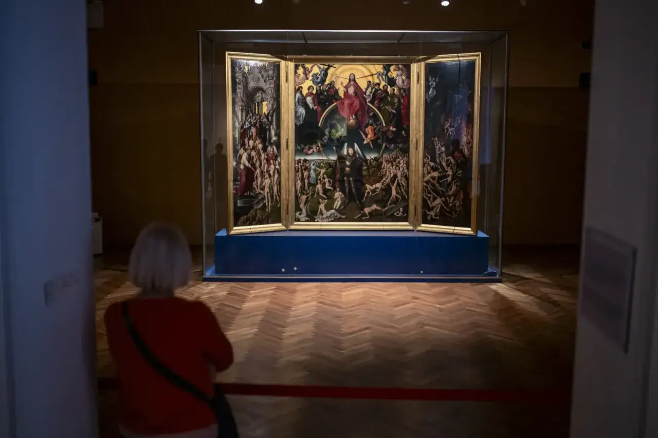 Widok na tryptyk w muzeum sztuki dawnej Gdańsk. Kobieta w czerwonej bluzce ogląda dzieło przedstawiające Sąd Ostateczny.