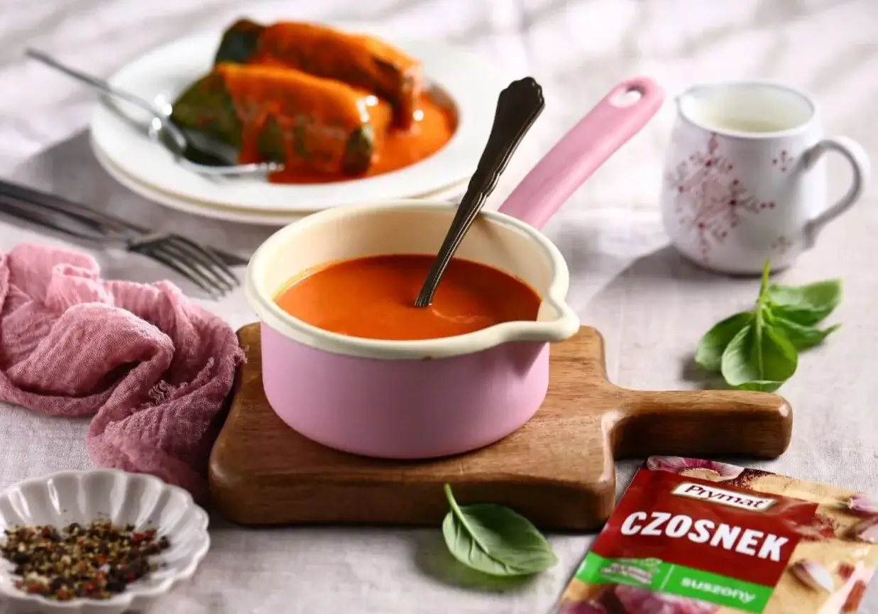 Aromatyczny sos do gołąbk&oacute;w w r&oacute;żowej rondelku, obok przyprawy z czosnkiem i świeżej bazylii.