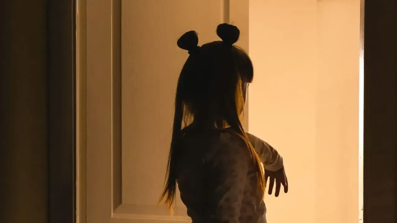 Dziecko w piżamie z dwoma kucykami na głowie stoi w drzwiach, zastanawiając się, dlaczego dziecko lunatykuje.