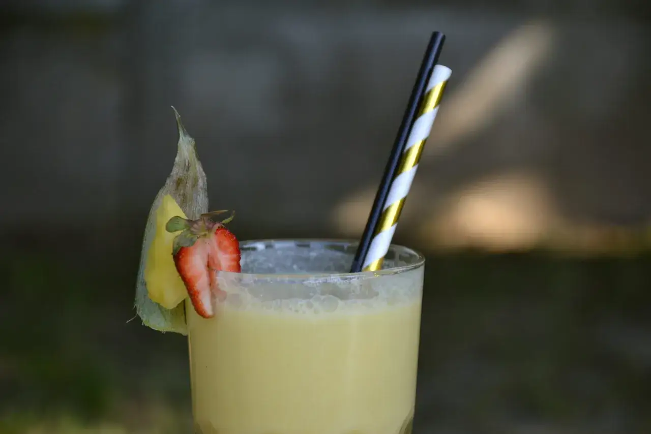 Orzeźwiający drink pina colada z kawałkiem ananasa i truskawką, ozdobiony słomkami.