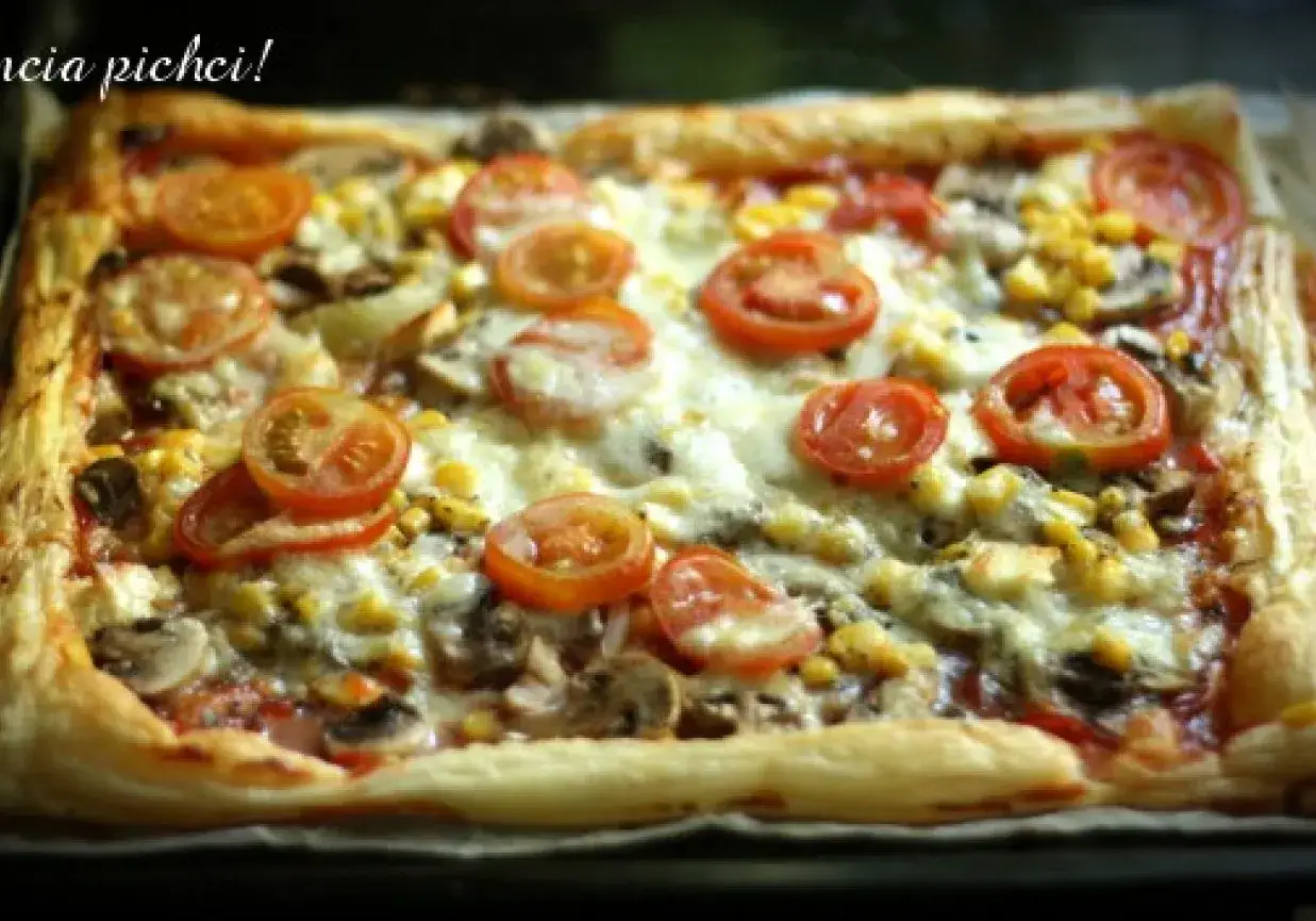 Pyszna pizza na cieście francuskim z pomidorkami, kukurydzą i pieczarkami, zapieczona pod ciągnącym serem.