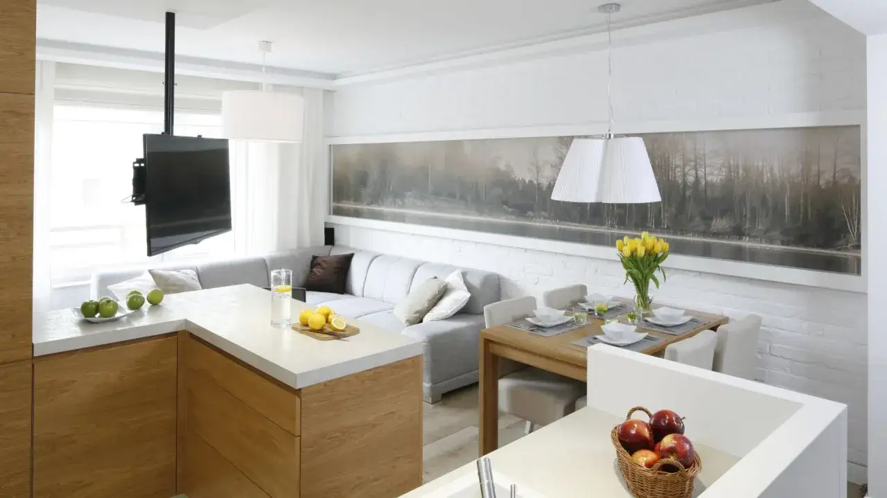 Nowoczesne mieszkanie w bloku: kuchnia z wyspą, szara kanapa, stół z krzesłami i duży obraz z lasem.