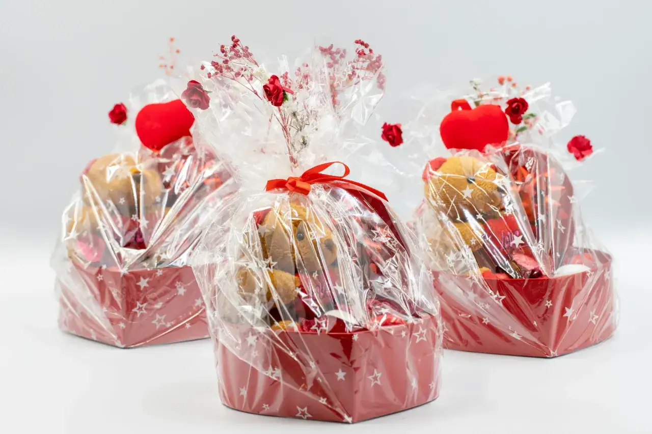 Trzy urocze koszyczki z pluszowymi misiami i czerwonymi serduszkami, pięknie zapakowane w celofan. To świetny pomysł, jak kreatywnie zapakować prezent.