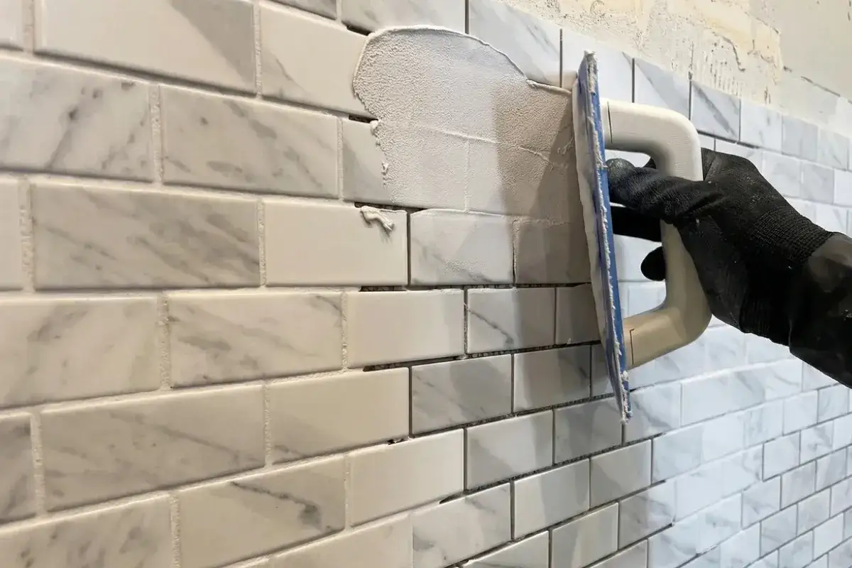 Ręka w rękawicy rozprowadza fugę epoksydową na marmurowej mozaice. Poradnik: fuga epoksydowa jak kłaść.