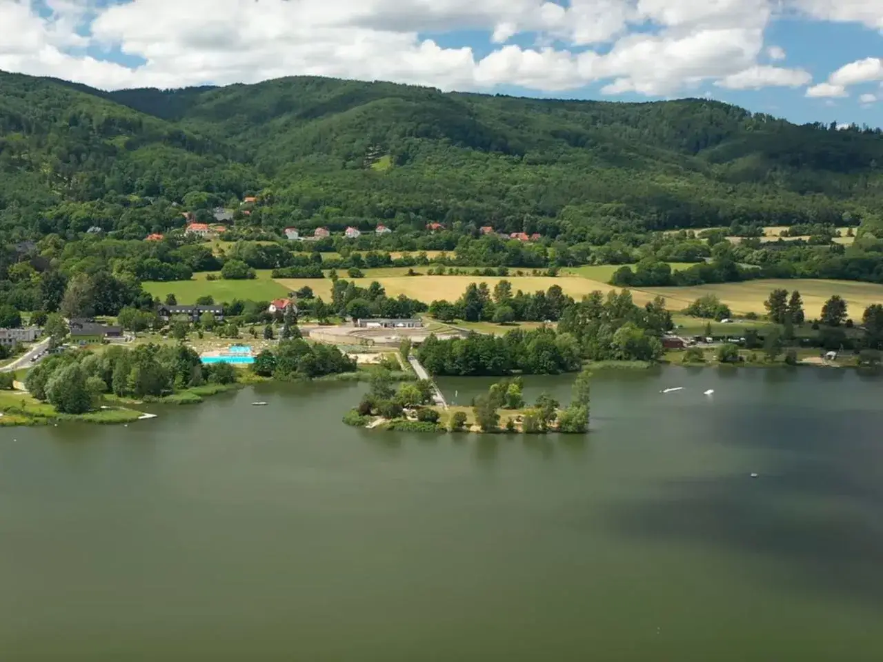 Jezioro Bielawskie oferuje liczne atrakcje: baseny, wyspy, a w tle zielone wzgórza i malownicze domy.