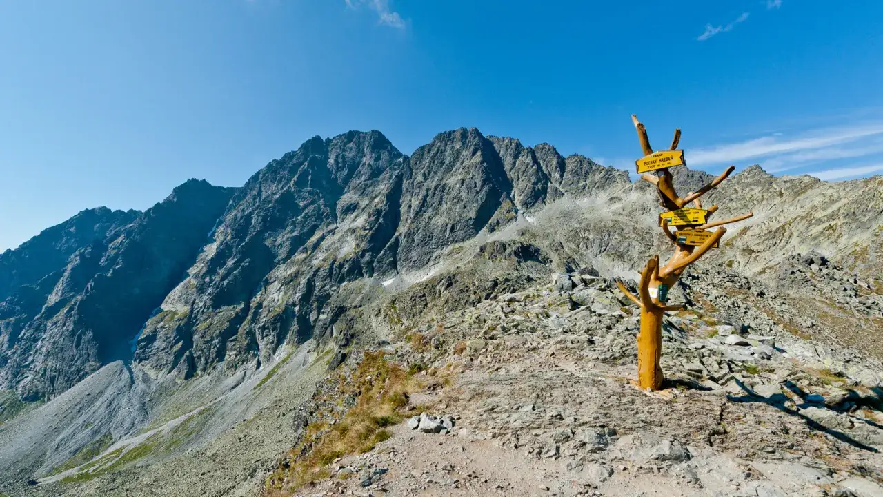 Słowackie Tatry, od kiedy otwarte szlaki, zapraszają na szczyty. Widok na skaliste g&oacute;ry i drewniany drogowskaz.