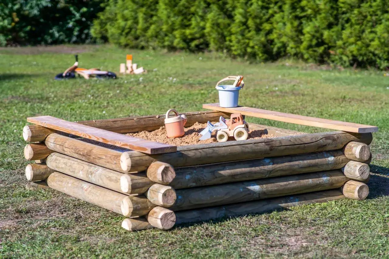 Drewniana piaskownica z zabawkami: wiaderko, łopatka i koparka. Idealna do zabawy na świeżym powietrzu, pokazuje, jak zrobić piaskownicę.