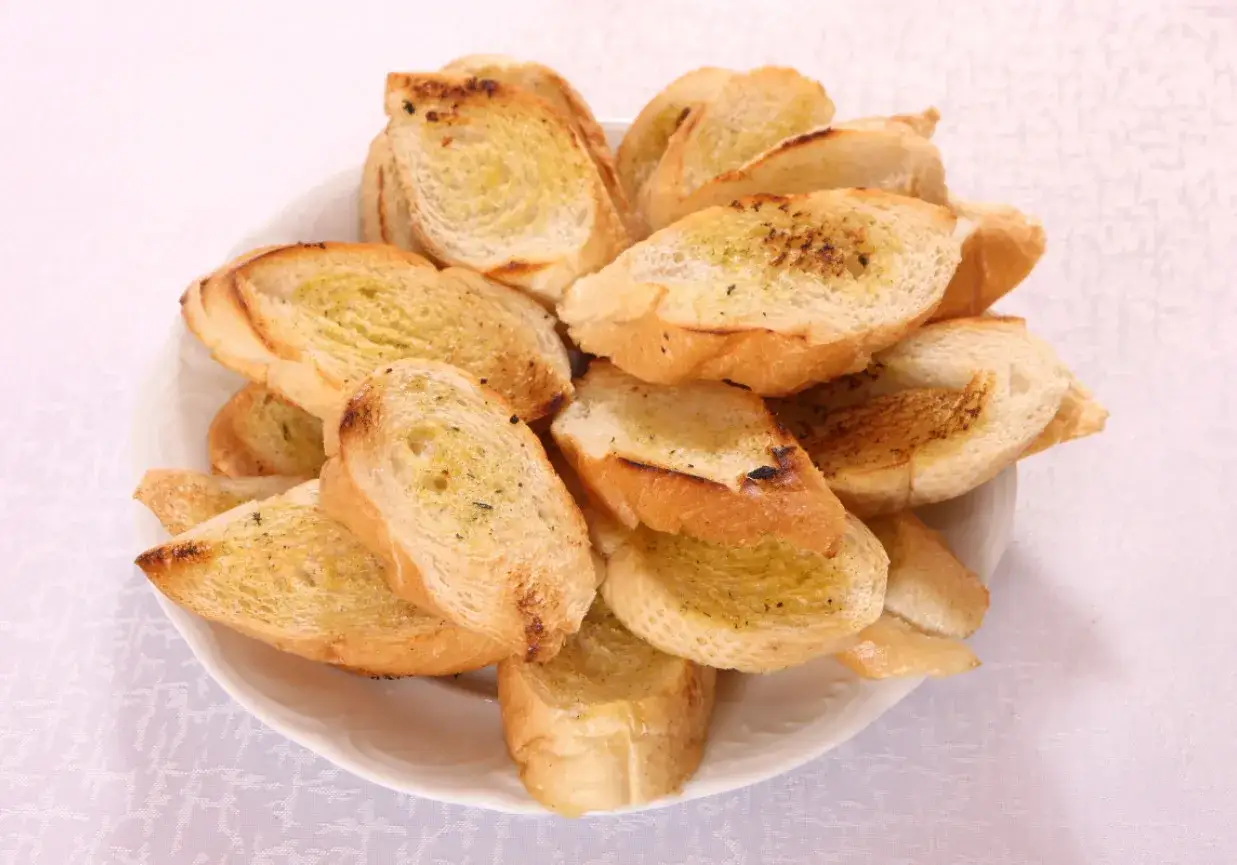 Stos pysznych, złocistych grzanek z piekarnika, posypanych ziołami, czeka na spr&oacute;bowanie.