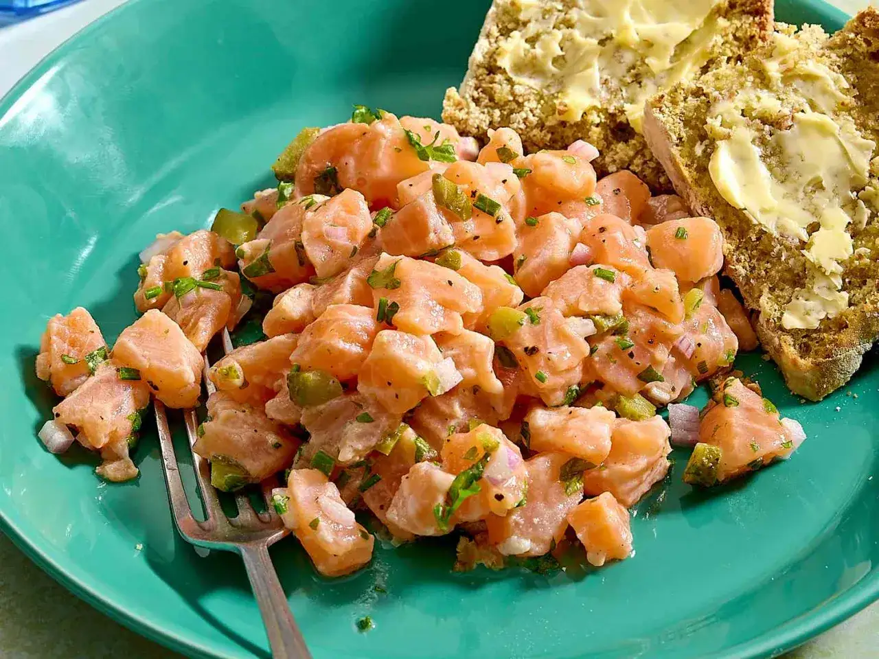 Pyszny tatar z łososia z dodatkiem szczypiorku i cebuli, podany z kromkami chleba z masłem.