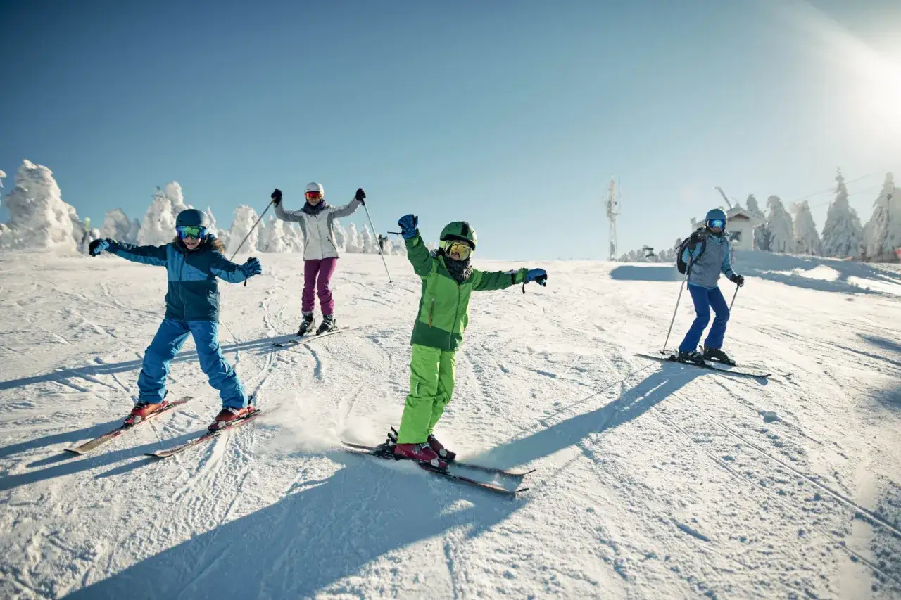 Dzieci szusują na nartach po ośnieżonym stoku, ciesząc się zimową przygodą. Idealne miejsca na ferie zimowe!