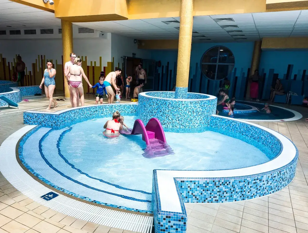 Rodzina cieszy się wodnymi atrakcjami w aqua parku Bukowina. Dzieci bawią się w basenie ze zjeżdżalnią, a dorośli relaksują się w wodzie.