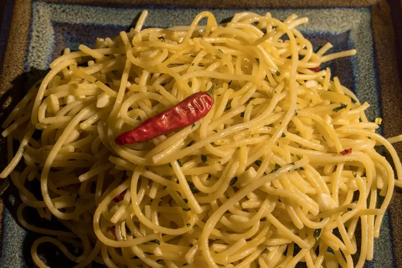 Spaghetti aglio olio z czosnkiem, natką pietruszki i ostrą papryczką na talerzu.