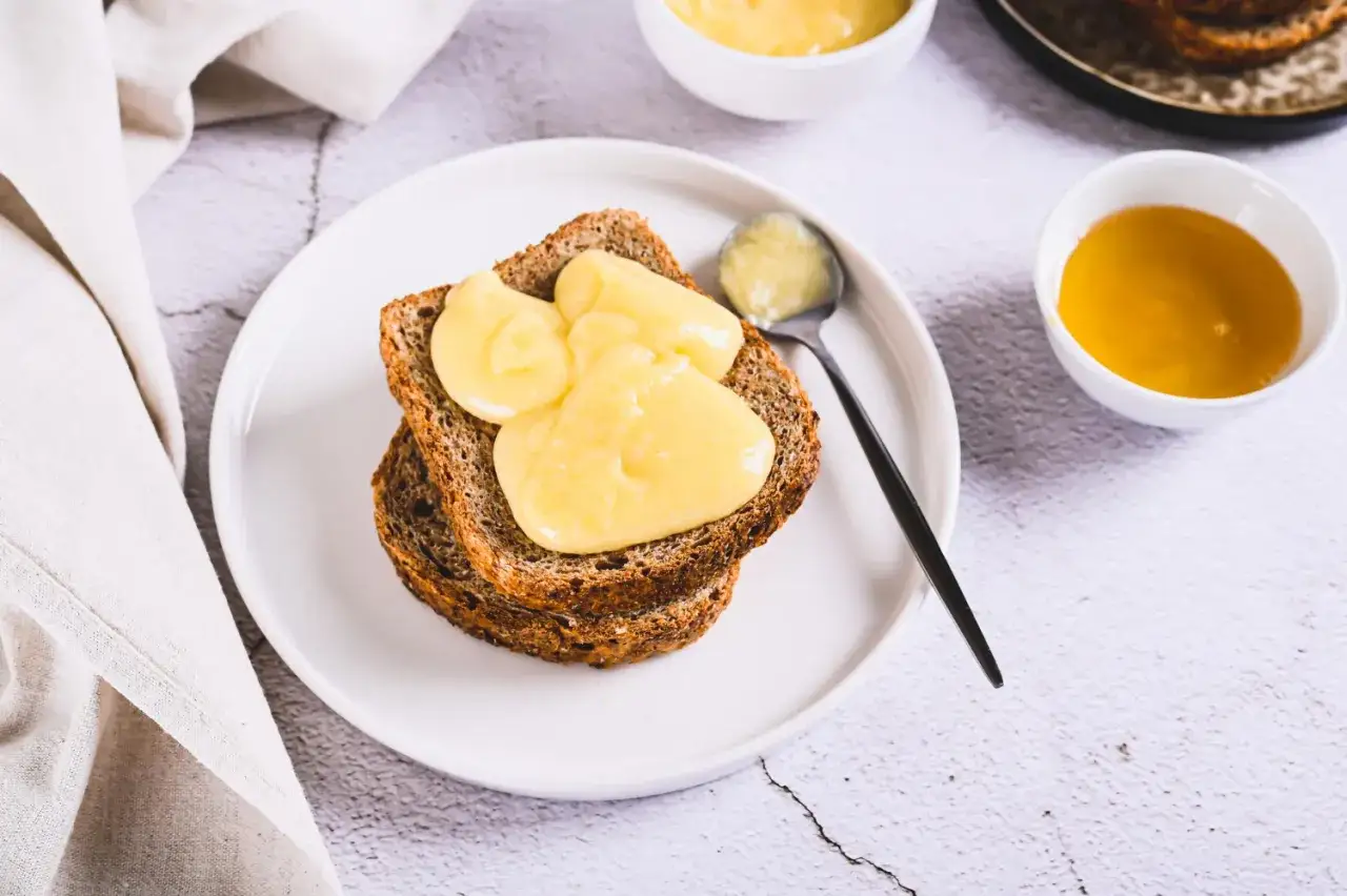 Na talerzu tost z kremem. Obok miseczka z płynnym złotym miodem, kt&oacute;ry nie jest wegański.