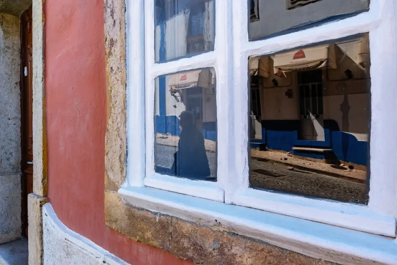 Zabytkowe okna drewniane odbijają ulicę i przechodnia.