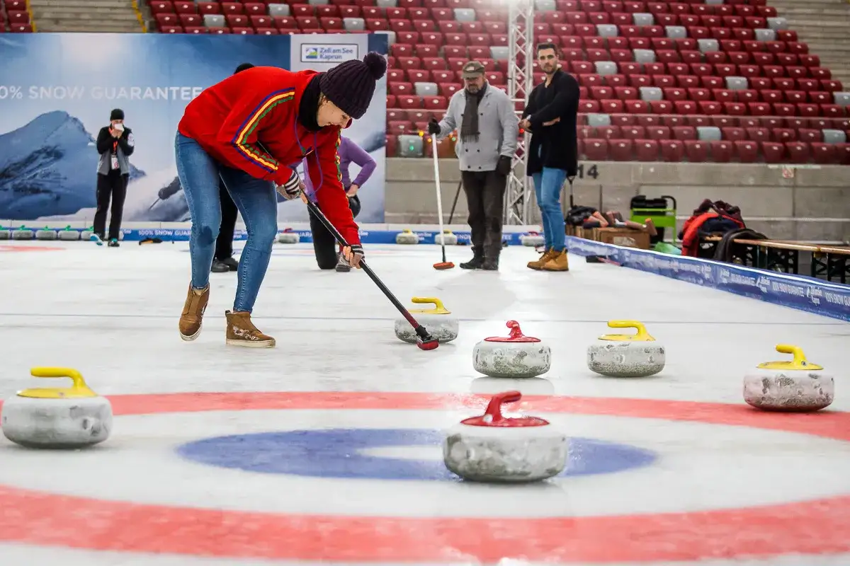 Kobieta w czerwonej bluzie i czapce ćwiczy rzuty kamieniem na lodzie. To fascynująca dyscyplina sportowa na lodzie, wymagająca precyzji i strategii.