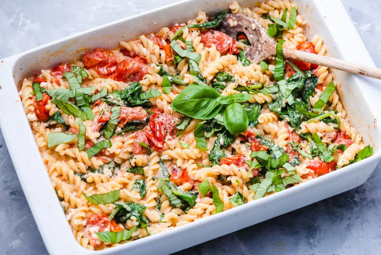 Pyszny makaron ze szpinakiem i fetą, zapieczony w białym naczyniu, udekorowany świeżą bazylią.