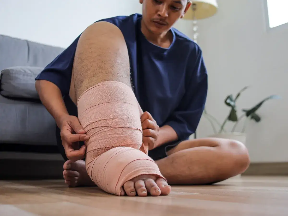 Mężczyzna bandażuje opuchniętą nogę, szukając domowych sposobów na opuchnięte nogi.