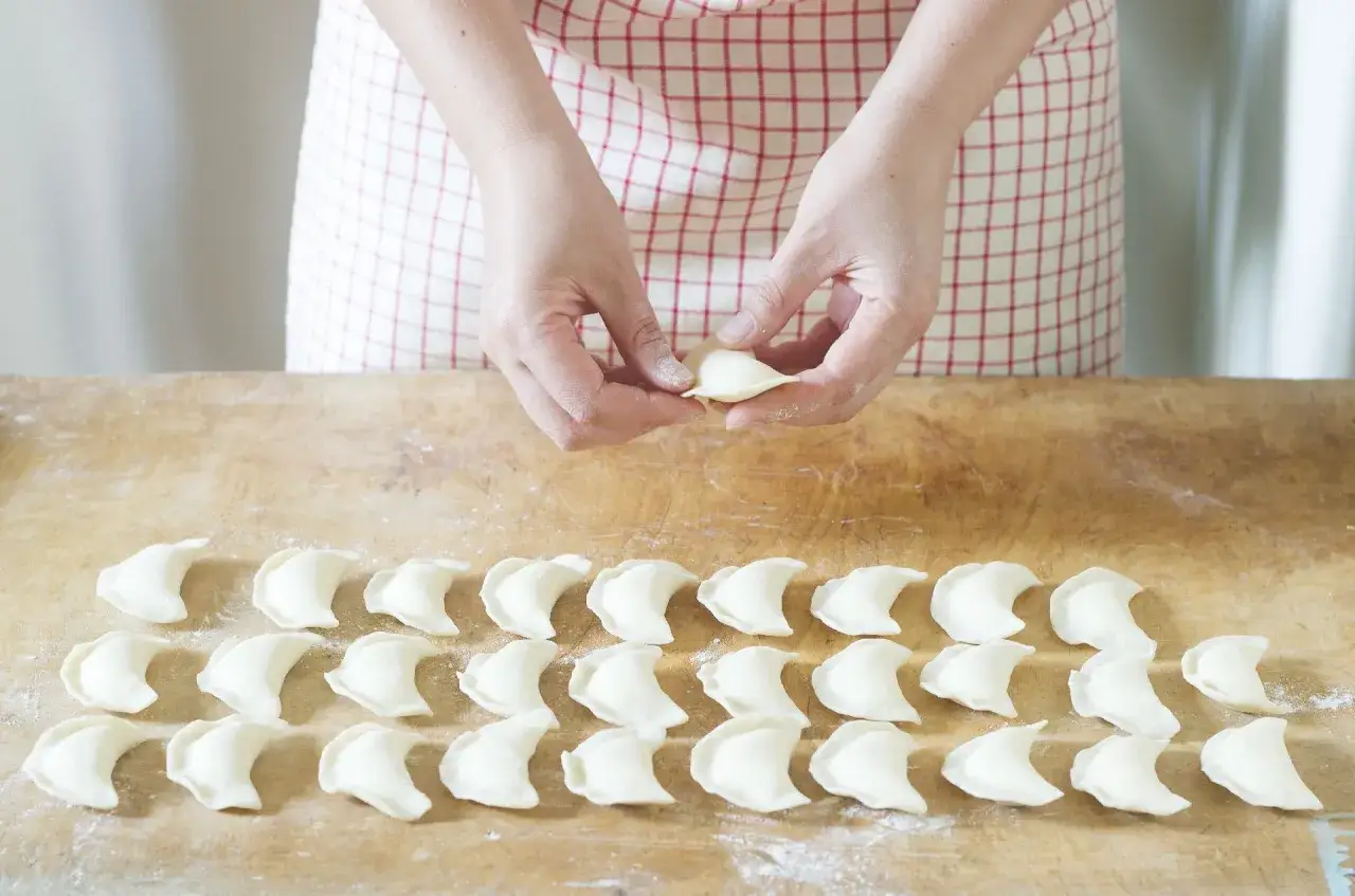 Ręcznie lepione pierogi na drewnianej desce. Zastanawiasz się, ile wychodzi pierogów z kilograma mąki? Oto odpowiedź w postaci gotowych do gotowania przysmaków.